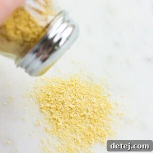 Freshly made vegan parmesan cheese being sprinkled from a container onto a rustic marble background, highlighting its fine, crumbly texture.