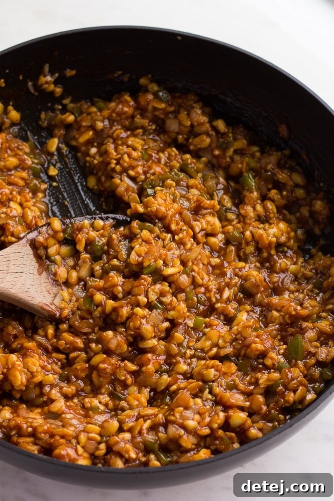 Cooked BBQ tempeh mixture in a skillet with a wooden spoon.