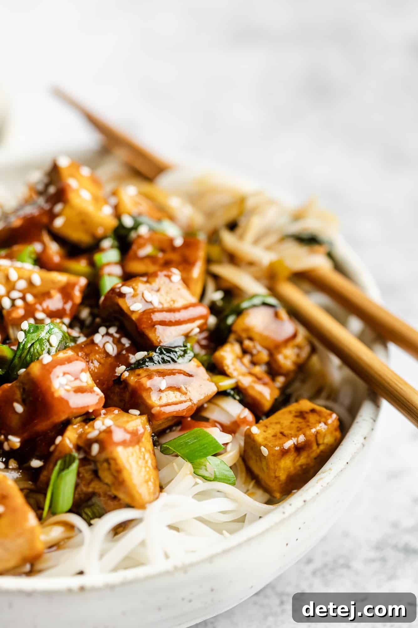 Effortless One Pan Tofu Stir Fry 2 close up on tofu stir fry over rice noodles in a bowl with chop sticks.