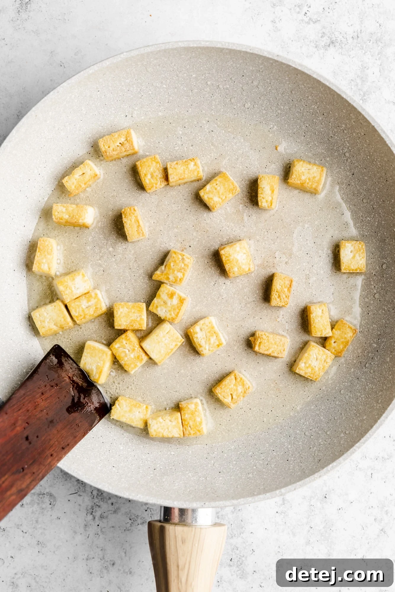 Effortless One Pan Tofu Stir Fry 4 golden brown tofu cubes frying in a grey skillet.