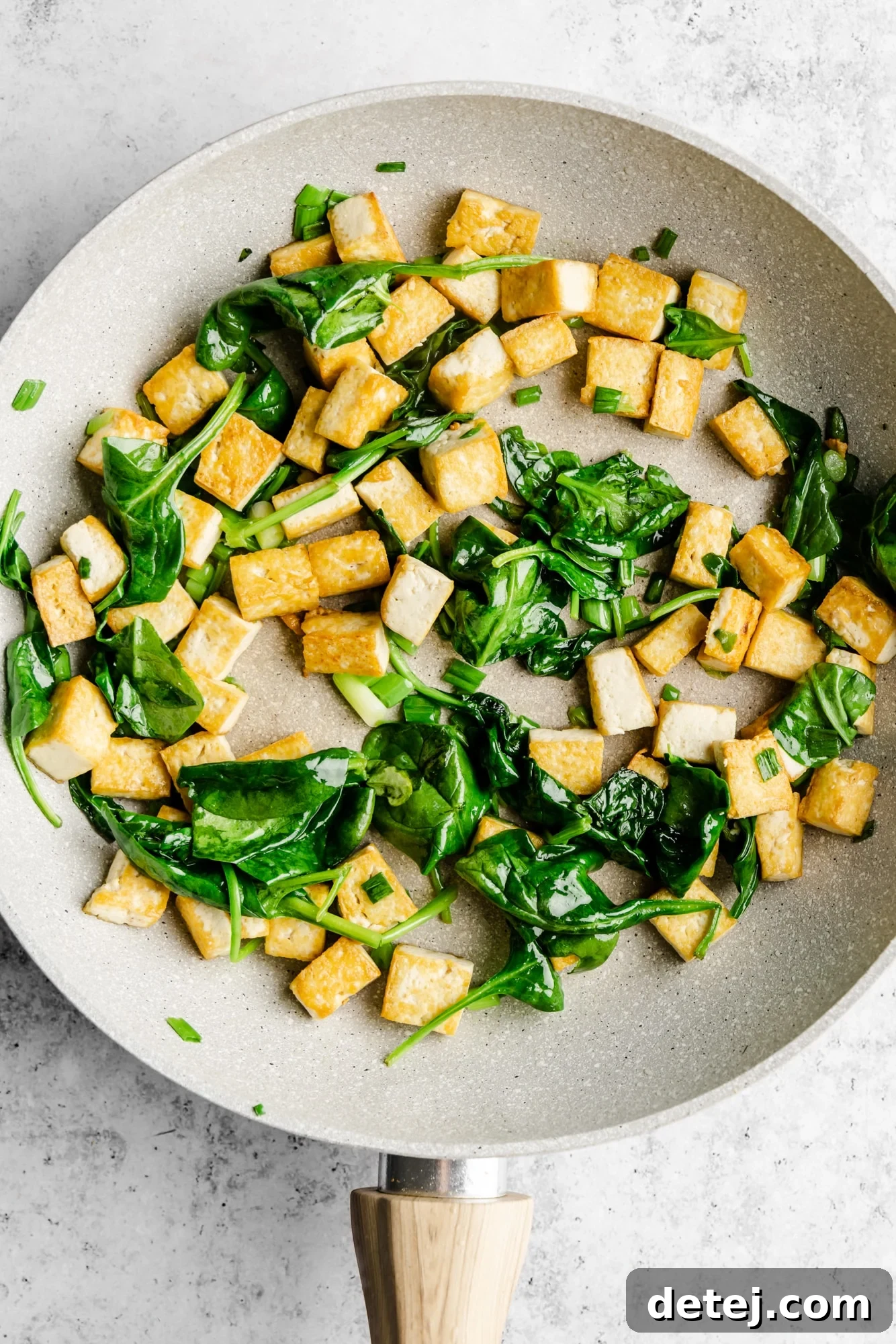 Effortless One Pan Tofu Stir Fry 5 tofu cubes and spinach frying in a grey skillet.