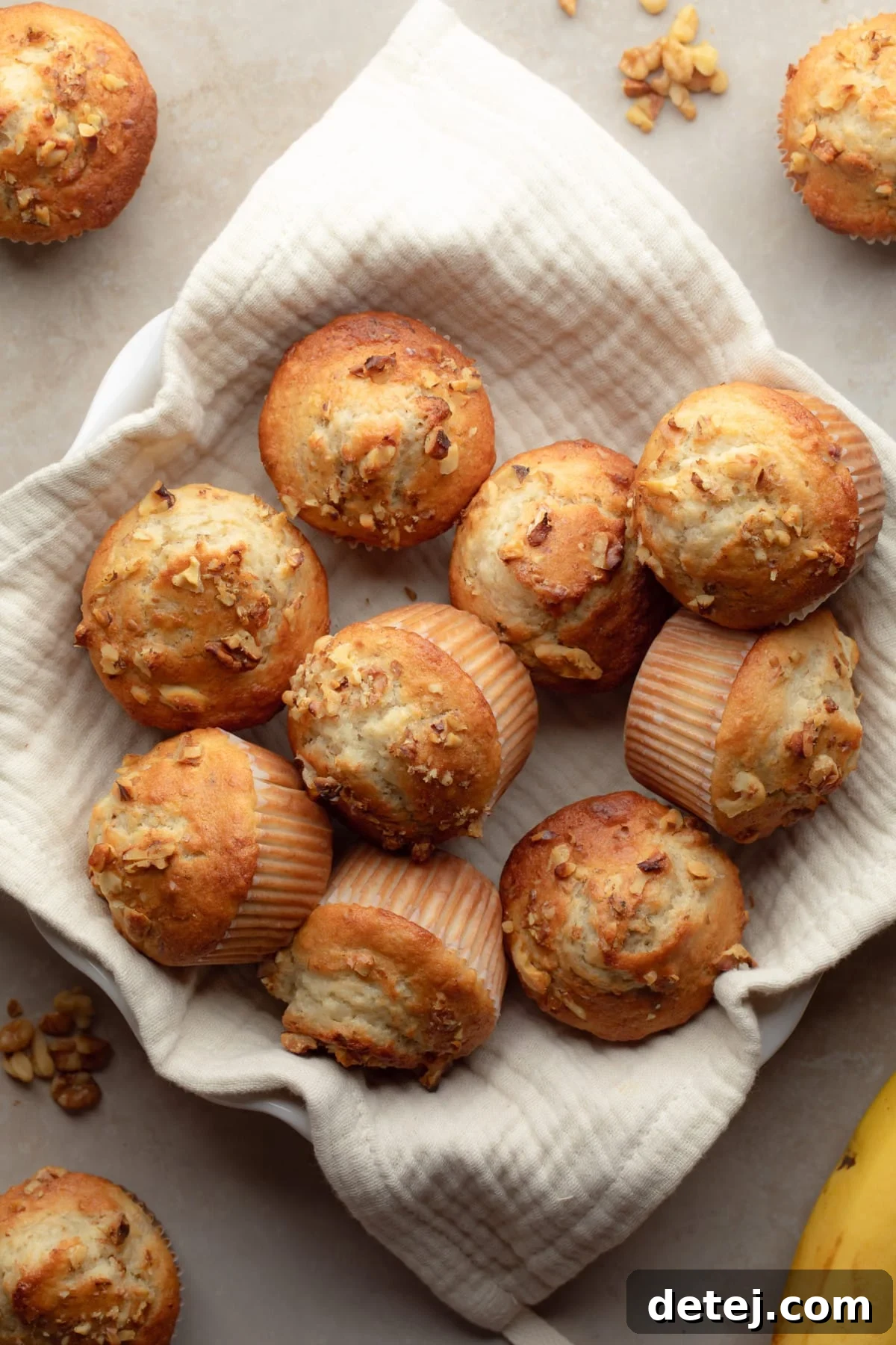 A rustic bowl filled with golden-brown vegan banana muffins, surrounded by more muffins on a cream towel.