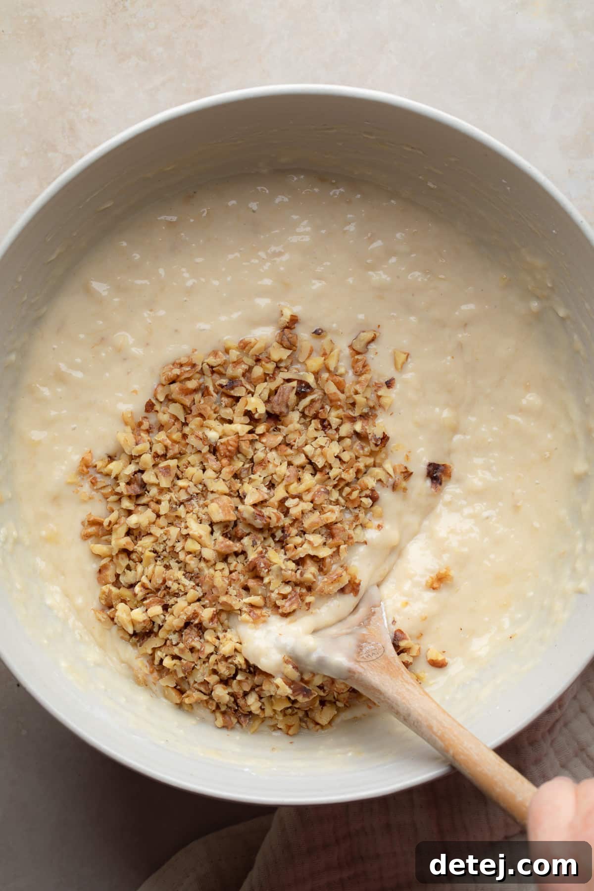 A bowl of vegan banana muffin batter with chopped walnuts folded in, ready for baking.
