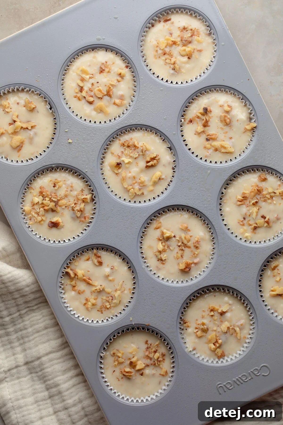 Unbaked vegan banana muffins in a lined muffin tin, topped with walnuts, ready to go into the oven.