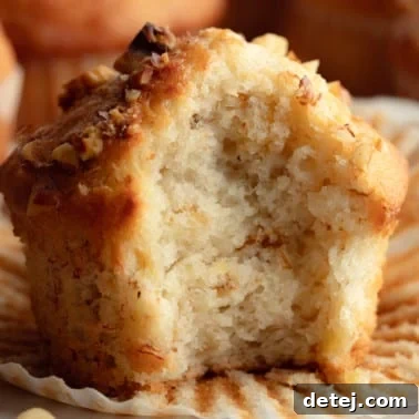 Square image of a close-up of a golden vegan banana muffin with nuts, with a bite taken out.