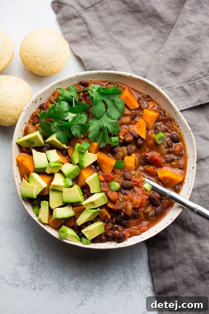 bowl of chili with sweet potatoes, avocado and cilantro on top, grey towel and background