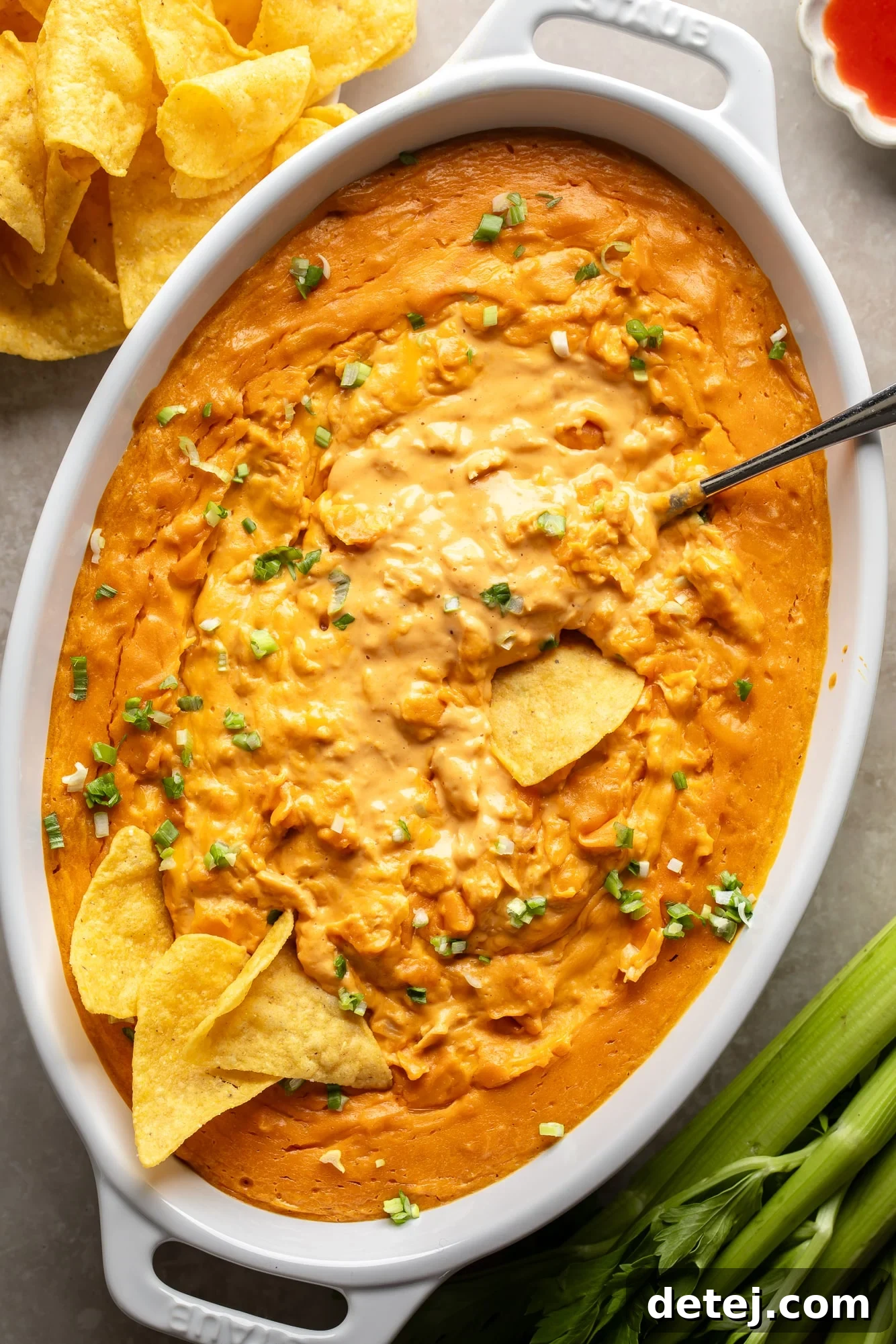 Overhead view of creamy vegan buffalo chicken dip in a large white baking dish, surrounded by tortilla chips, ready for serving.