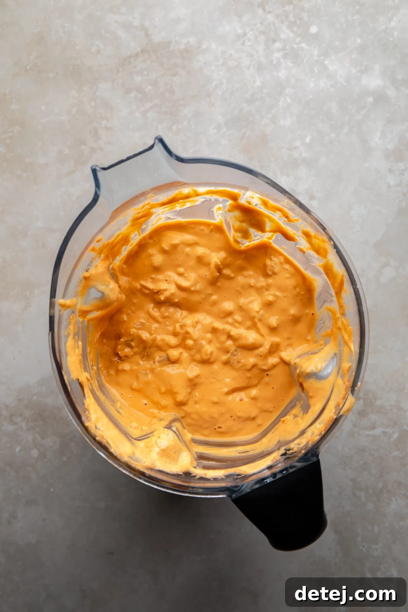Chunky blended orange vegan buffalo chicken dip in a blender, showing the desired textured consistency.