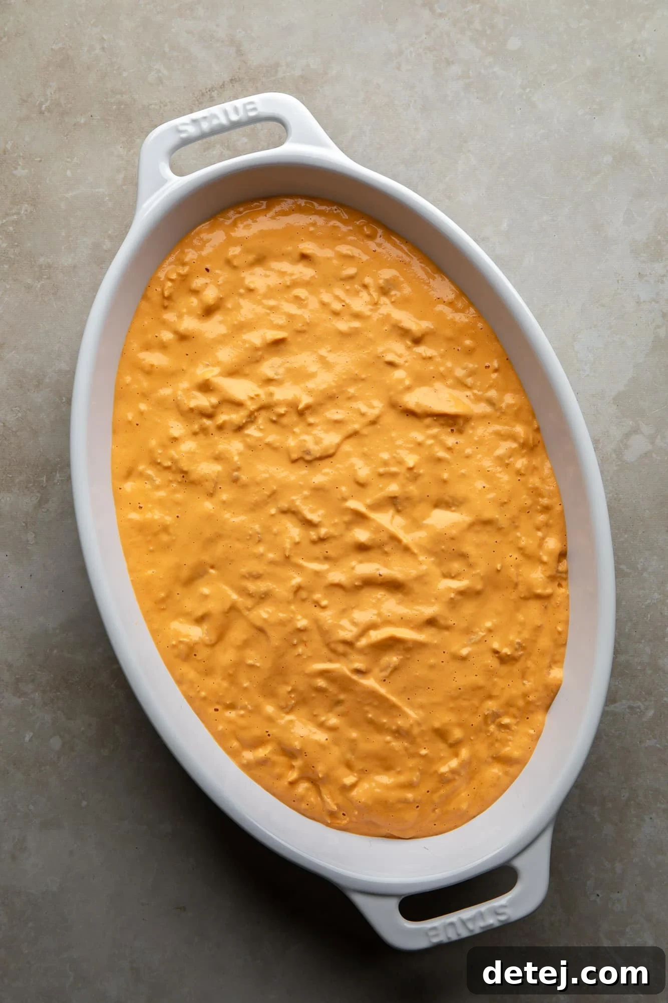 Warm, bubbly orange vegan buffalo chicken dip in a large white baking dish, fresh from the oven.
