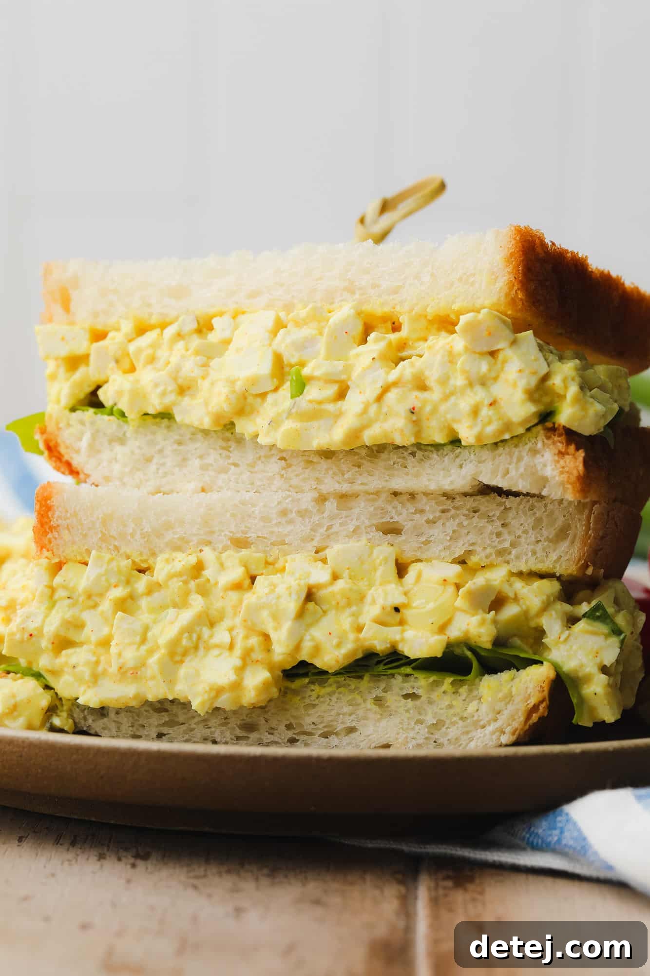 two vegan egg salad sandwiches piled on top of each other, showcasing the creamy filling and fresh bread.