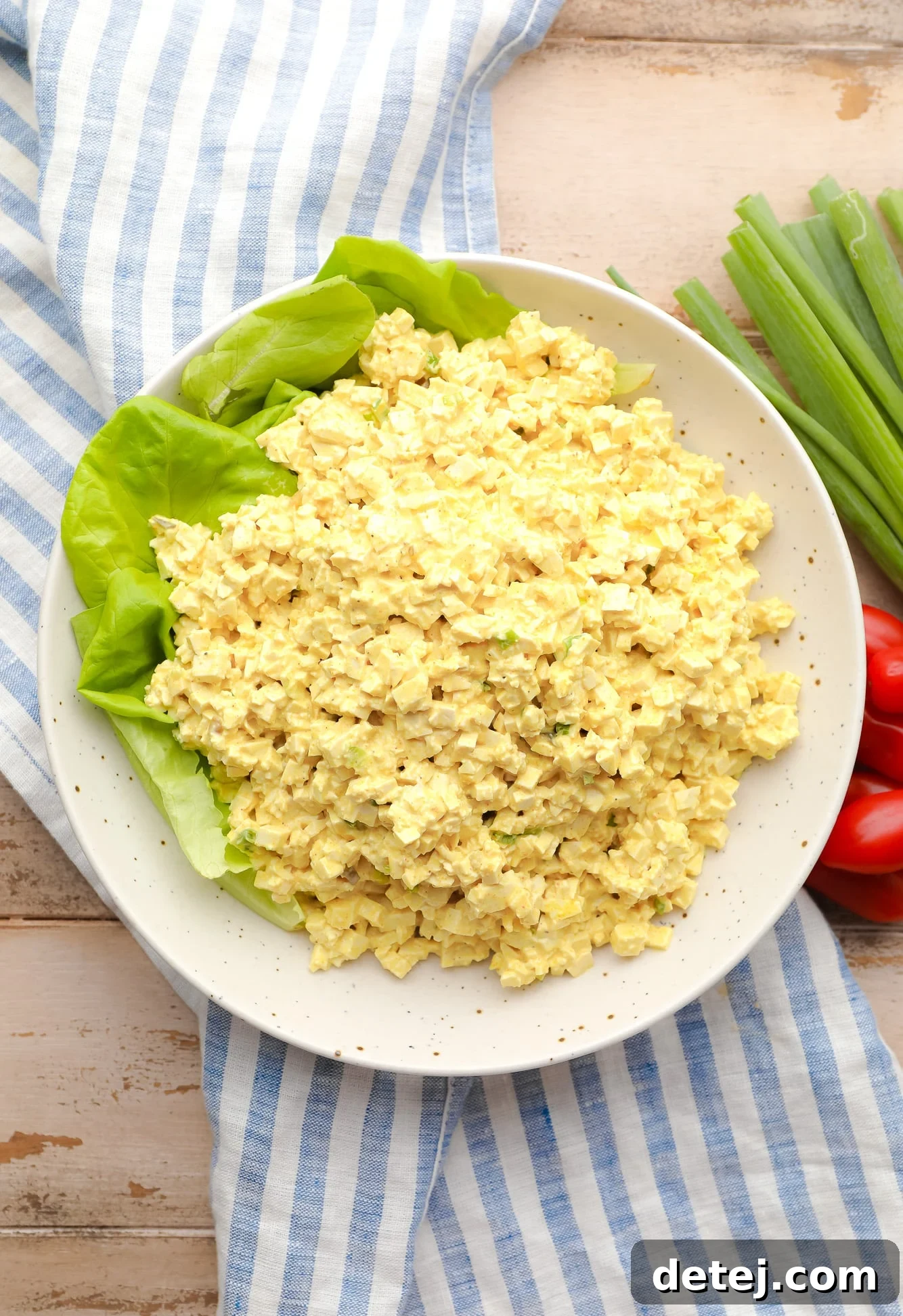 a large batch of vibrant vegan egg salad presented artfully on a spacious white plate, garnished with fresh herbs.