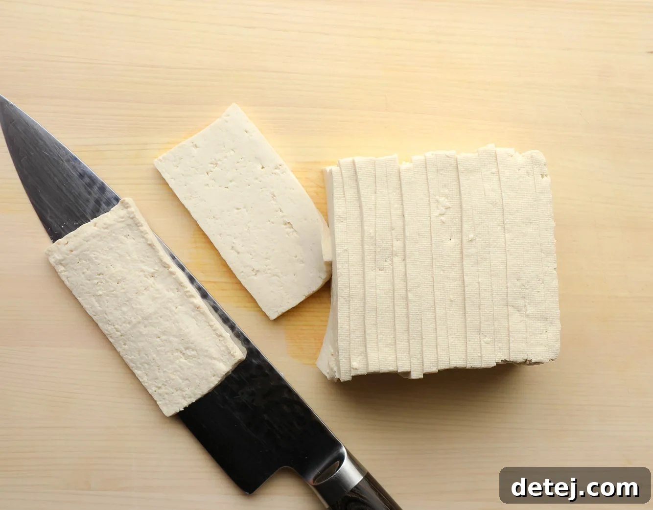 using a chef's knife to slice a brick of tofu into thin, rectangular strips, demonstrating the initial step of tofu preparation.