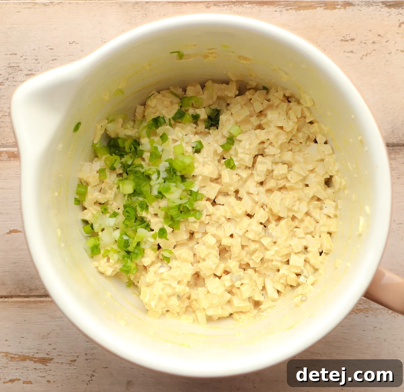 vegan egg salad topped with fresh scallions in a large white bowl, ready for serving.