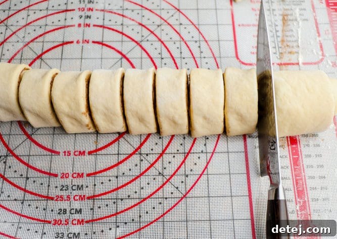A knife slicing the rolled dough into individual cinnamon rolls.