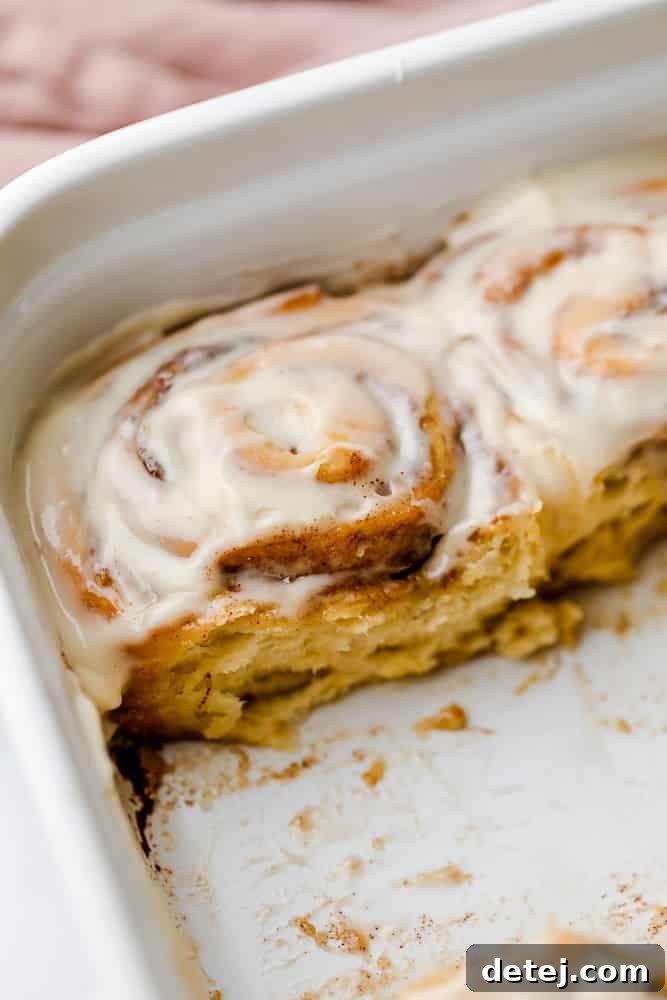 A casserole dish with baked cinnamon rolls, some already taken out, showing their soft interior.