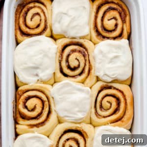 Square image of frosted vegan cinnamon rolls in a white dish