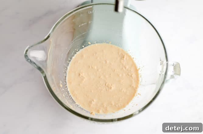 Foamy yeast mixture in a stand mixer bowl, indicating active yeast.