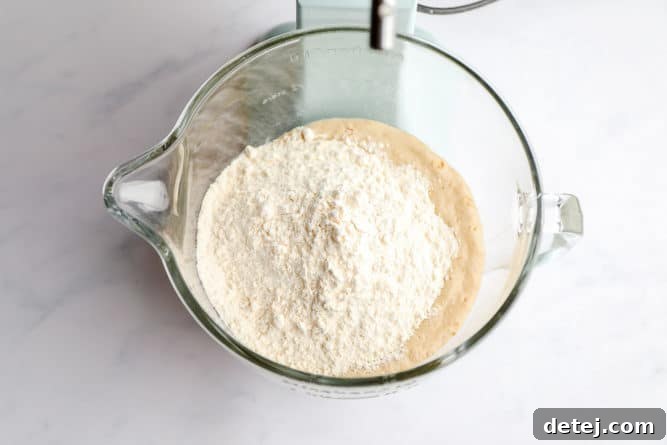 Flour being added to the wet ingredients in a stand mixer, starting the dough formation.