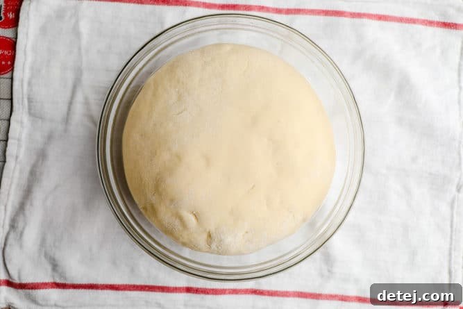 A ball of risen dough, covered with a red striped towel, in a glass bowl.