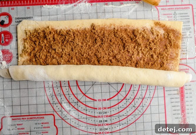 Dough being tightly rolled up with the cinnamon and brown sugar filling visible.