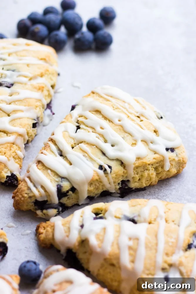 Two glazed vegan blueberry scones presented on a clean grey background, showcasing their perfect shape and glistening glaze.