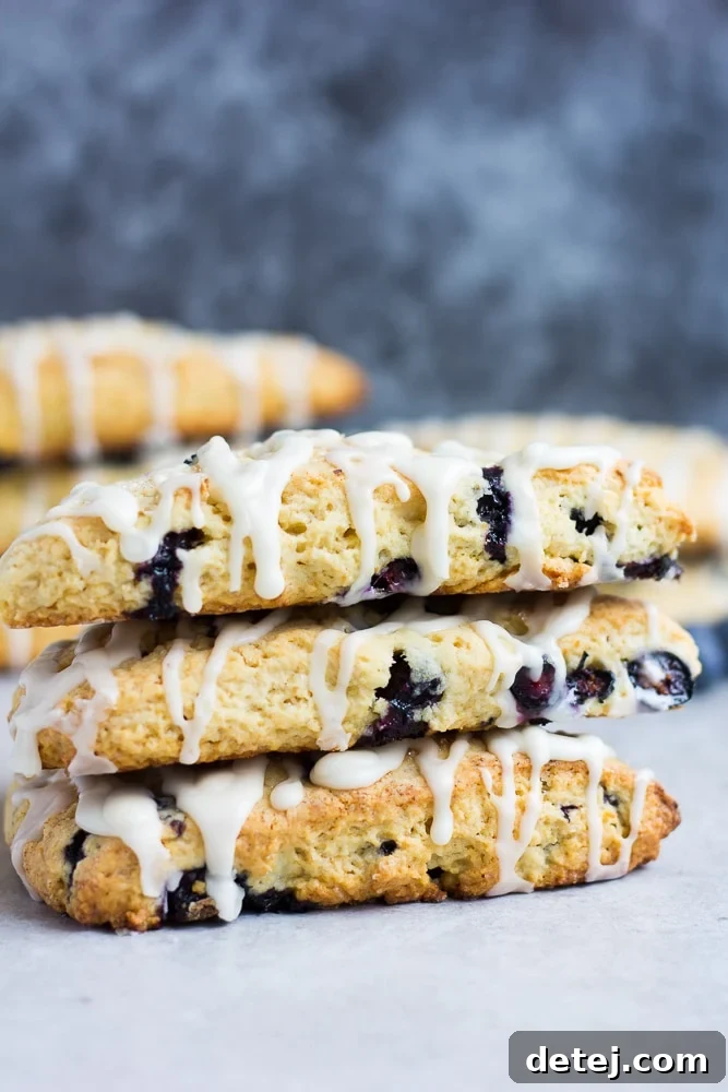 A stack of three perfectly baked vegan blueberry scones, showcasing their golden crust and juicy blueberry filling.