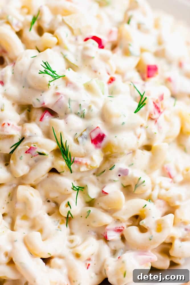 A super close-up view of the vegan macaroni salad, highlighting the perfectly cooked noodles, vibrant red bell peppers, fresh green dill, and the luscious creamy dressing.