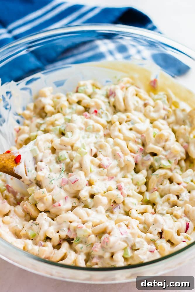 Close-up of creamy macaroni salad being stirred in a bowl, showing the rich texture and vibrant ingredients melding together.