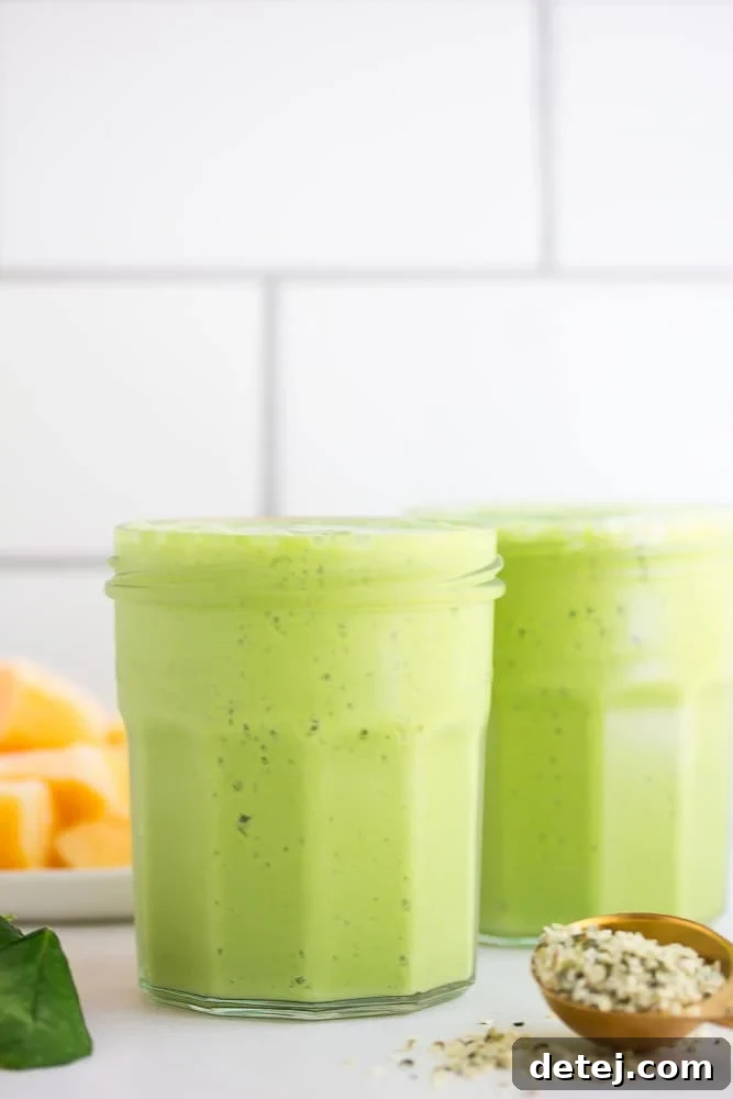 Two glasses of vegan green smoothie with fresh mango slices on a tiled background, showcasing a healthy and refreshing drink.