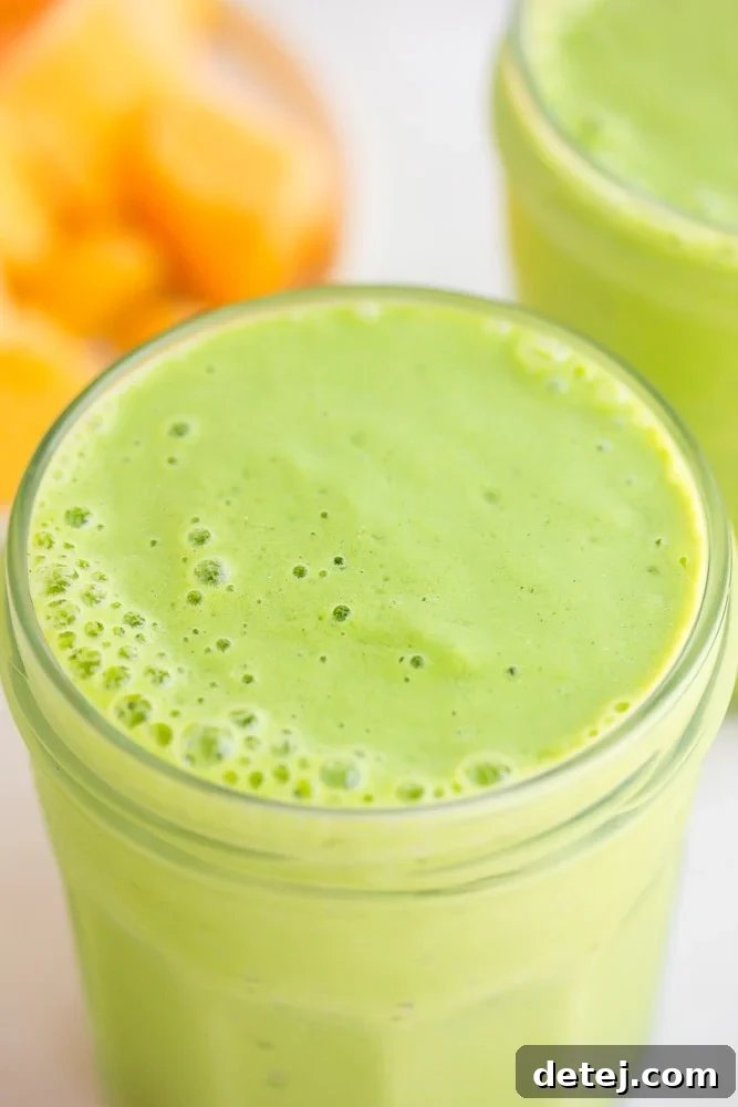 Close-up view of a refreshing vegan green smoothie, with a blurred background of fresh mango slices, emphasizing its natural ingredients and appealing texture.