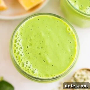 looking down close up on vegan green smoothie with mango and leaves in background.