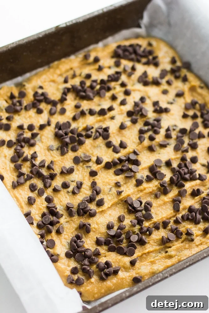 unbaked chickpea blondies in a parchment-lined pan, topped with chocolate chips