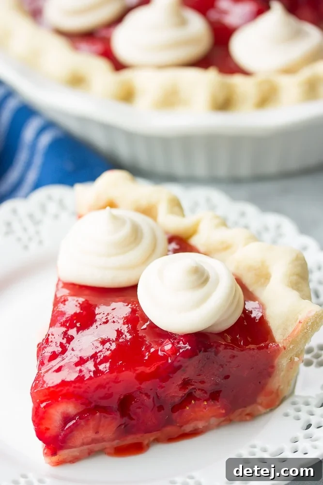 slice of strawberry pie on a white plate, blue towel in background.