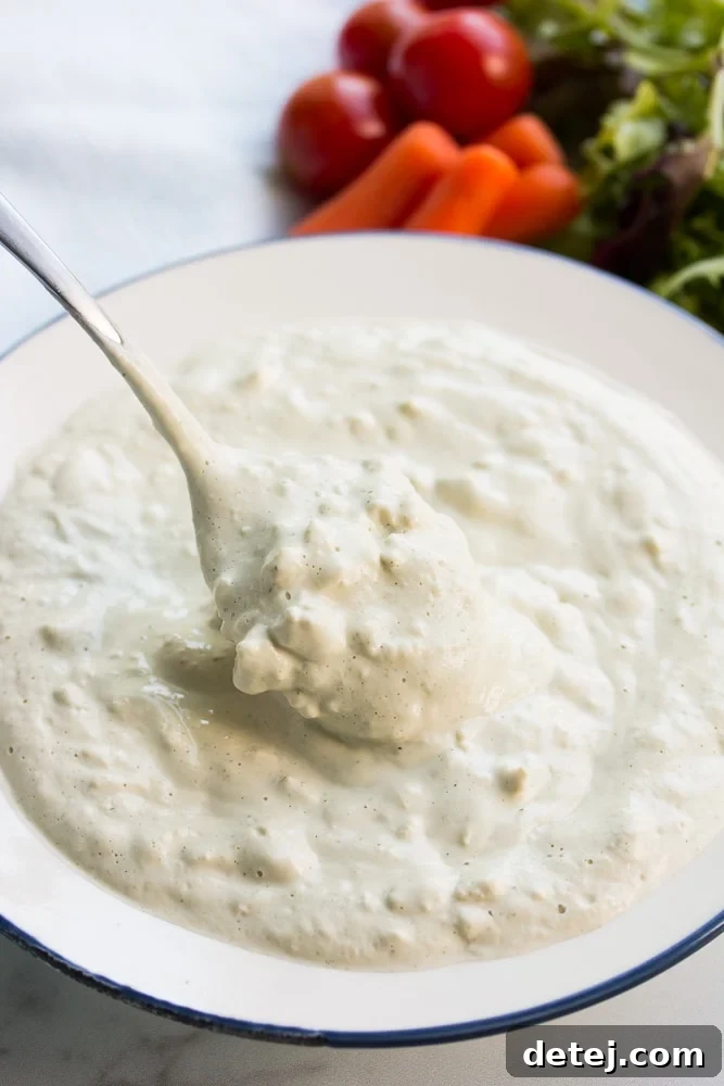 Creamy vegan blue cheese dressing with visible chunks, a spoon is lifting some from a bowl.