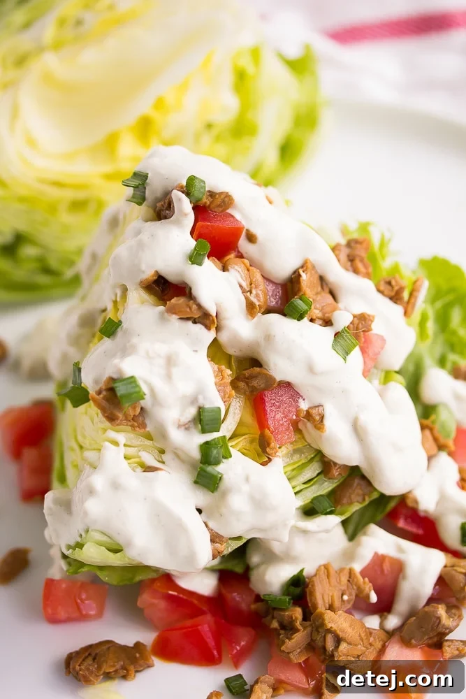 A vibrant vegan wedge salad featuring iceberg lettuce, diced tomatoes, tempeh bacon, and a generous drizzle of homemade vegan blue cheese dressing.