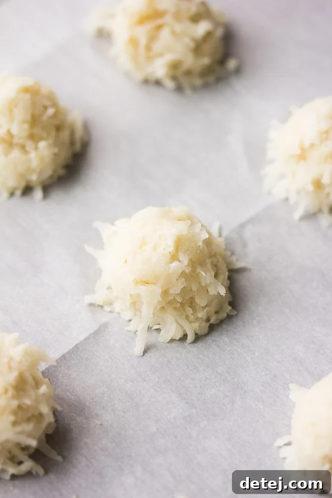 Unbaked mounds of vegan coconut macaroon dough neatly arranged on a parchment-lined baking sheet, ready for the oven.