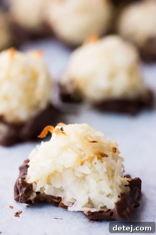 A vegan coconut macaroon with a bite taken out of it, revealing its moist and chewy interior, set against a dark background.