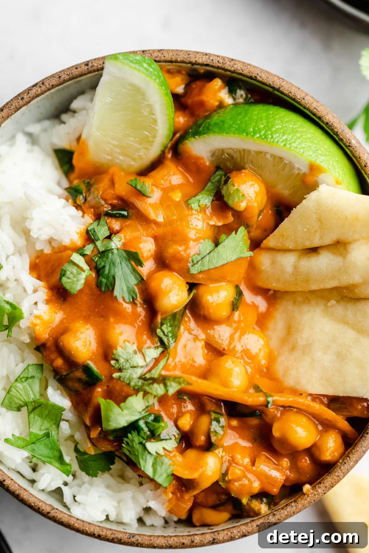 A beautifully presented bowl of creamy chickpea curry with rice, naan bread, and fresh cilantro garnish, set against a white background.
