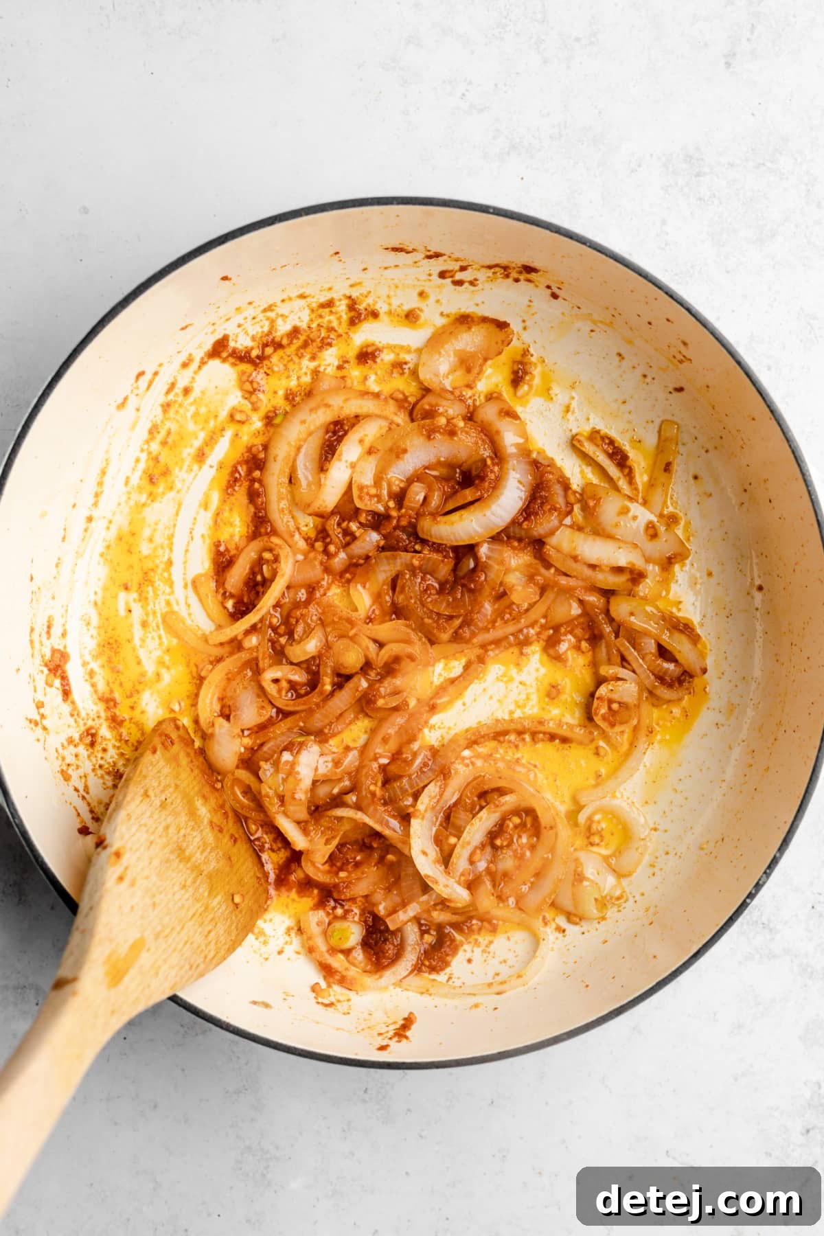 Onions and minced garlic being stir-fried in a pot with a wooden spoon, forming the aromatic base of the curry.