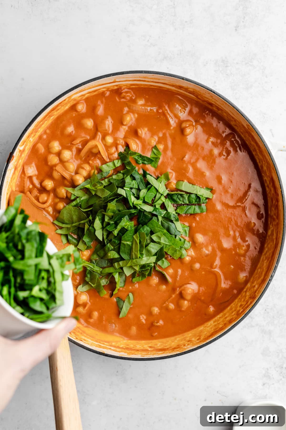 Adding fresh baby spinach to a simmering pot of chickpea and tomato curry, which will wilt into the sauce.