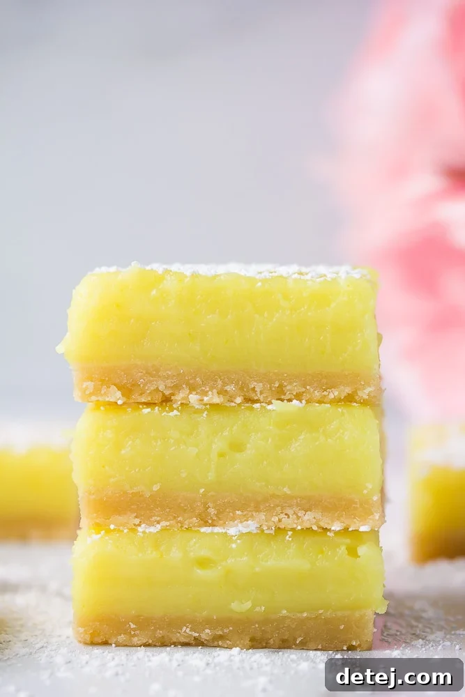 Stacked vegan lemon bars with delicate pink flowers in the background, showcasing their golden crust and creamy lemon filling.