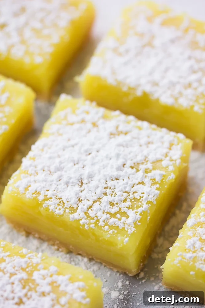 Close-up of freshly baked vegan lemon bars, neatly lined up and generously dusted with powdered sugar, ready to be enjoyed.