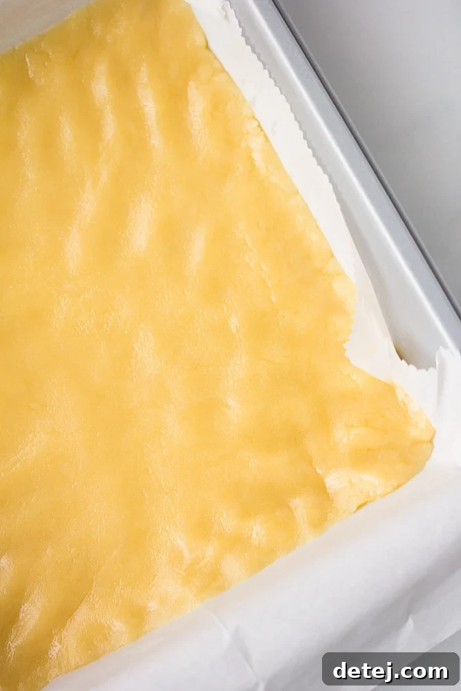 Close-up of the uncooked shortbread crust pressed evenly into a baking pan lined with parchment paper, prior to baking.