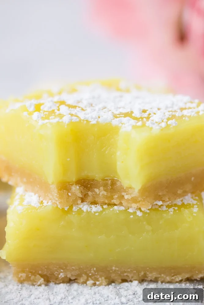Close-up shot of a vegan lemon bar with a bite taken out, revealing the creamy lemon layer and crumbly crust, with pink flowers blurred in the background.