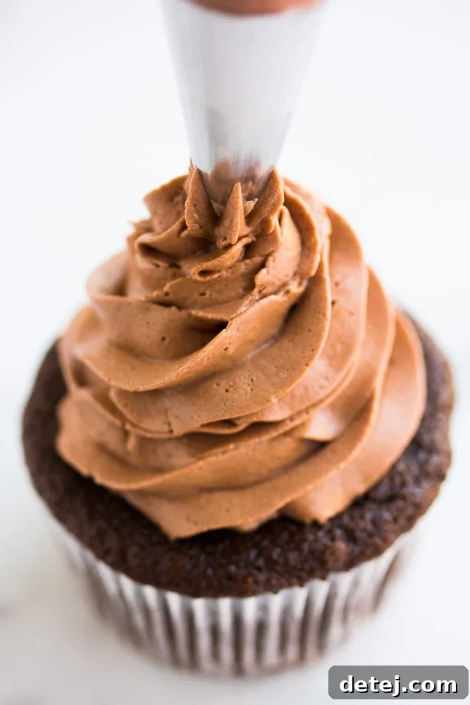 Rich vegan chocolate frosting being expertly piped onto a delicate cupcake, showcasing its smooth, creamy texture and perfect consistency for intricate decorations.