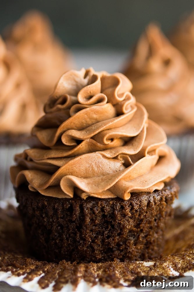 Close-up of a perfectly frosted vegan chocolate cupcake with its liner pulled down, revealing its moist crumb.