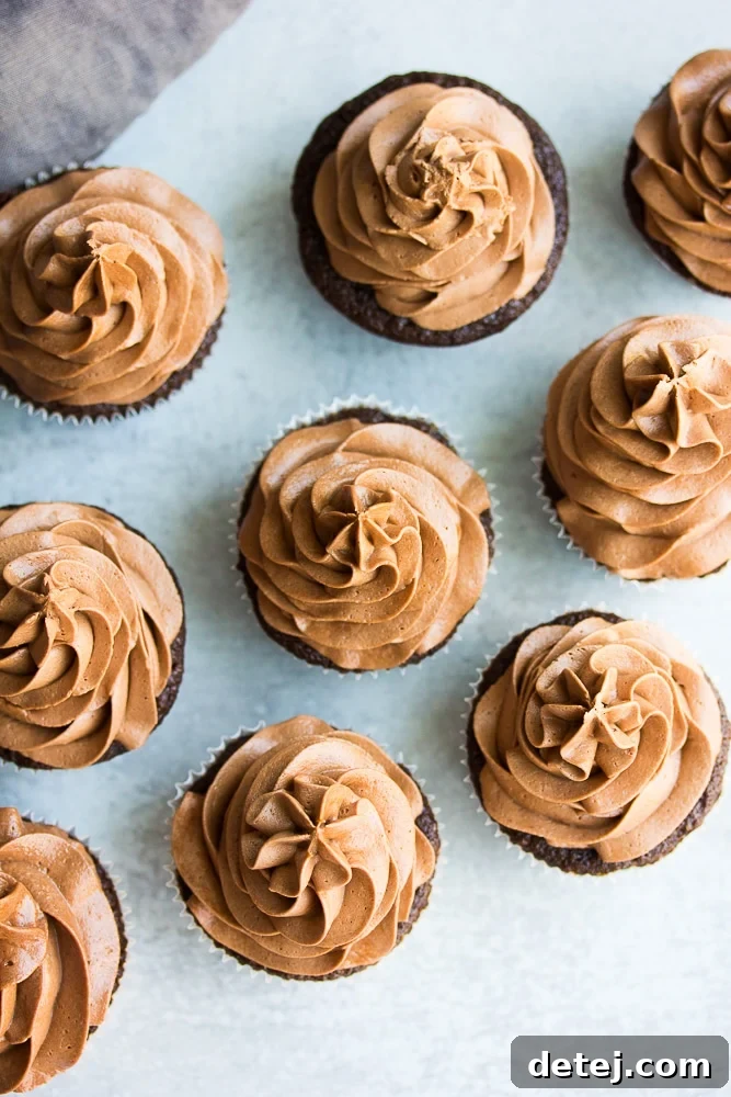 Overhead shot of several freshly baked vegan chocolate cupcakes, some frosted and some plain.