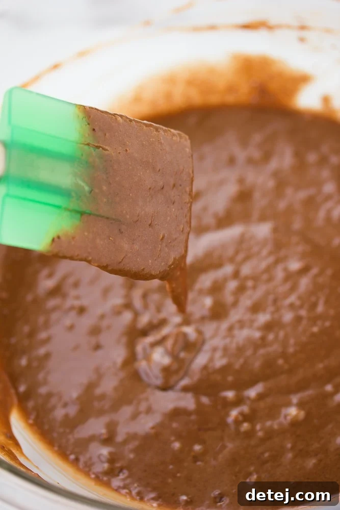 Chocolate cupcake batter in a large bowl with a green spatula, showcasing its smooth consistency.