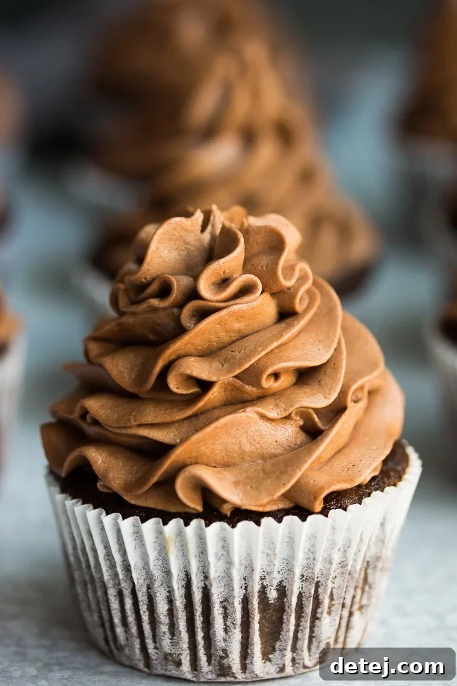 A close-up shot of a single vegan chocolate cupcake in a white paper liner, showing its rich, dark color and perfect rise.