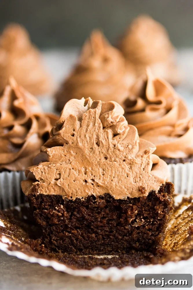A chocolate cupcake sliced in half to show its moist interior, with more frosted cupcakes visible in the soft focus background.